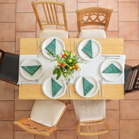 Image of a dining room table taken from above set with 6 places of white crockery and green serviettes no people or food